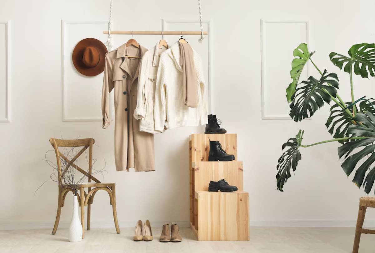 Stylish clothing hangs on a rack, with shoes on wooden blocks beside a plant and a chair, creating a chic interior scene.