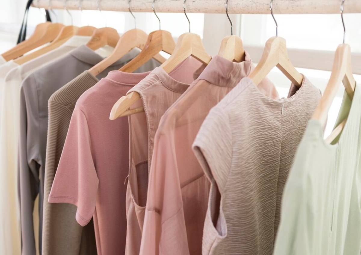 A clothes rack displaying a variety of pastel-colored tops in soft fabrics, including pink, beige, olive green, and light gray.
