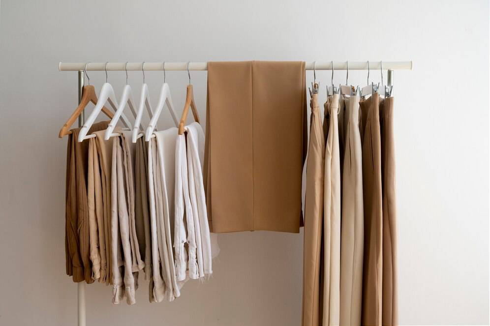 A clothing rack displays an array of neutral-toned pants and tops, hanging neatly in a stylish, minimalist setup.