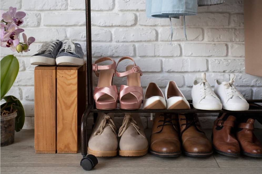 A stylish shoe wadorbe displays a variety of shoes, including sneakers, heels, and boots, beside a blooming orchid and wooden crates.