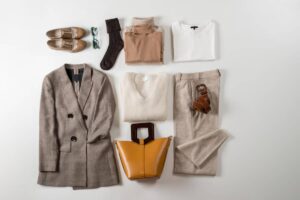 A neatly arranged flat lay of stylish clothing items including a brown blazer, sweaters, trousers, shoes, a handbag, and accessories.