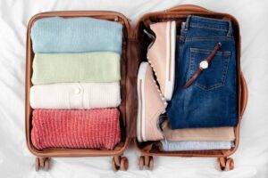 A neatly packed suitcase with folded sweaters, jeans, a watch, and a pair of light sneakers, ready for travel.