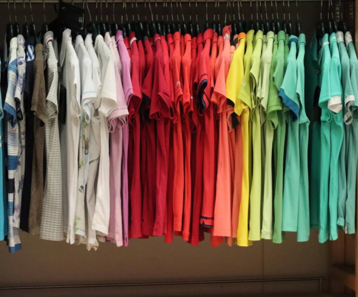 A colorful array of short-sleeved shirts hanging on hangers, displaying shades from blue and white to red, orange, yellow, and green.