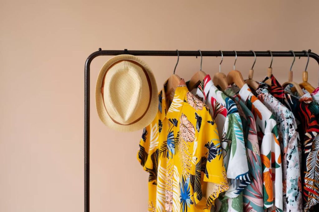 A stylishly arranged rack featuring colorful tropical shirts and a straw hat against a soft peach background.