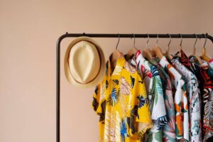 A stylishly arranged rack featuring colorful tropical shirts and a straw hat against a soft peach background.