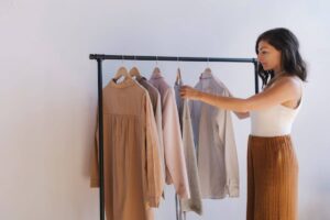 A woman selects clothes from a rack, showcasing various styles and colors against a minimalistic background.