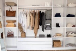 A neatly organized closet featuring clothing on hangers, shelves with bags, boxes, and folded items, creating a minimalist aesthetic.